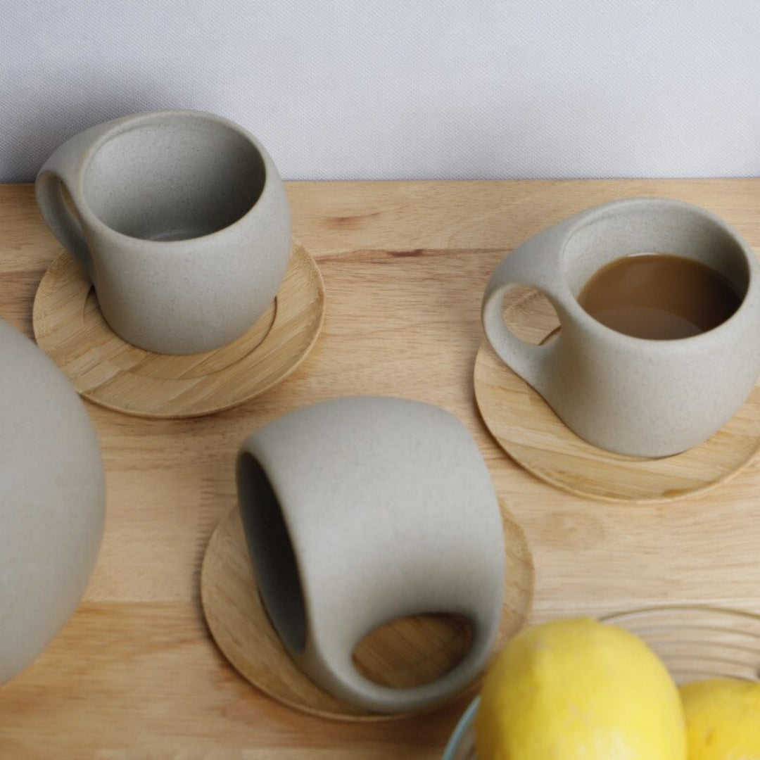 Three ceramic mugs on wooden coasters with a lemon on a wooden surface.