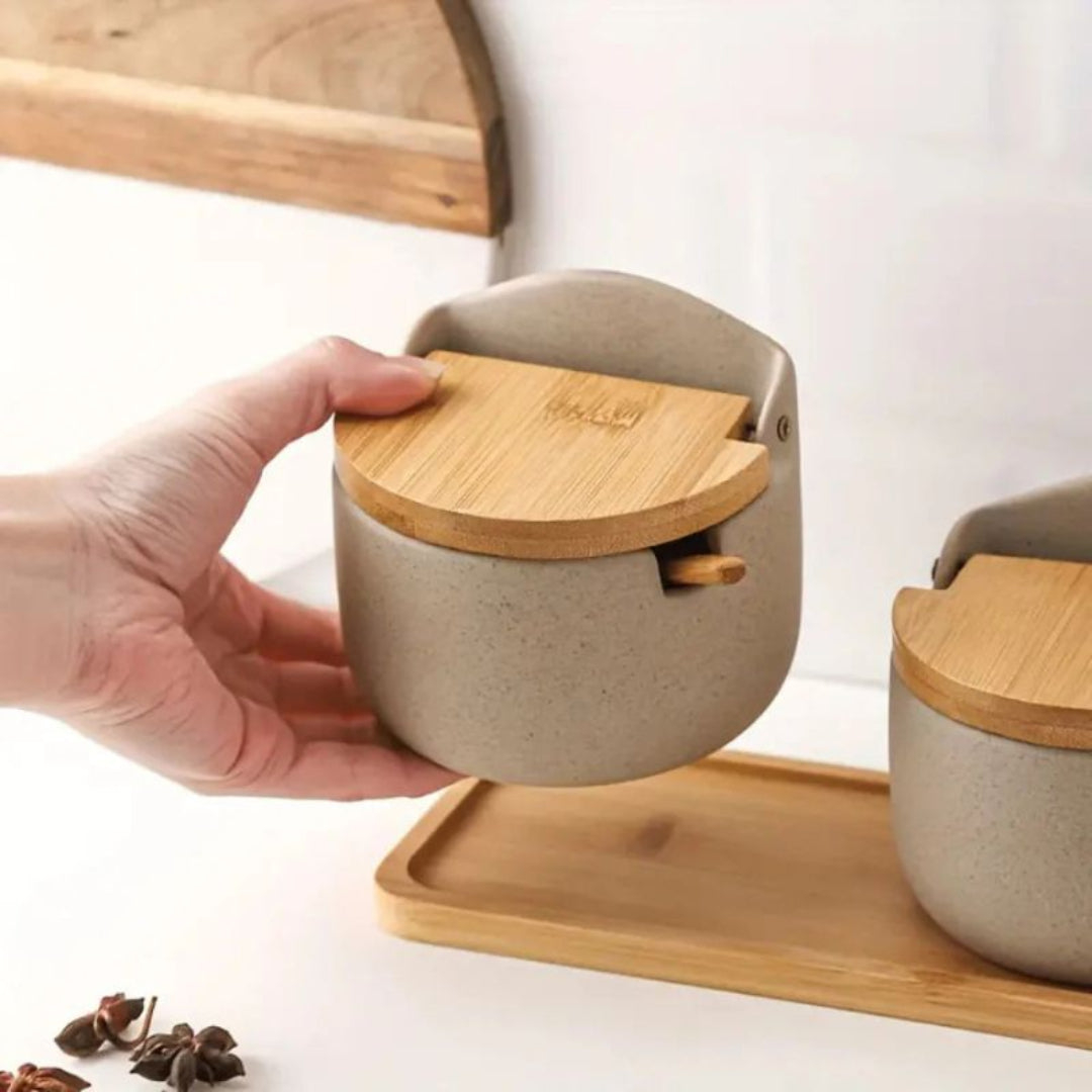 Hand holding a small beige container with a wooden lid on a white background