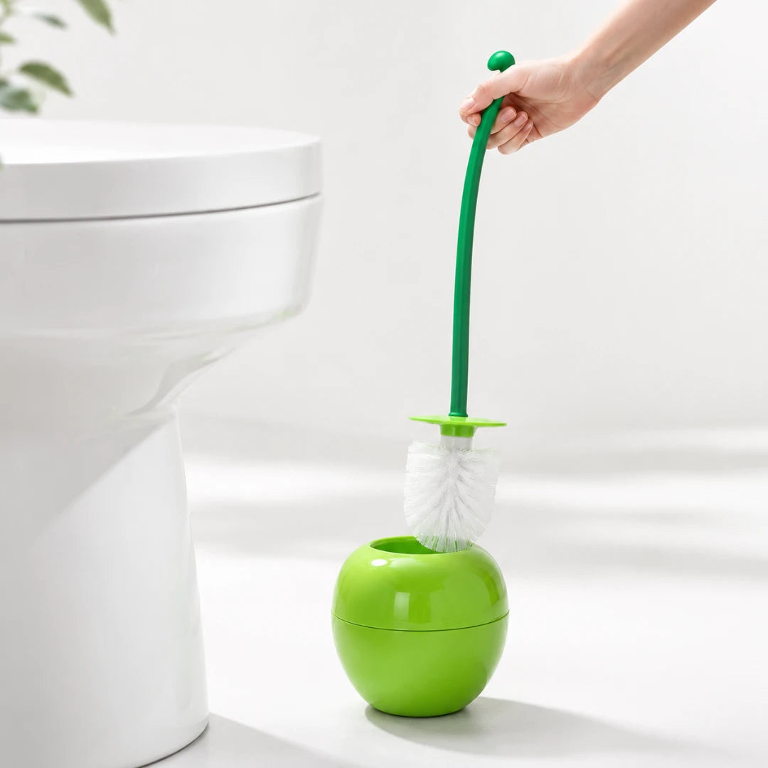 Josh & Tate - CherryPop™ Toilet Brush & Holder - A green toilet brush with a white bristle head and a matching green holder, shown beside a white toilet with a hand holding the brush handle.
