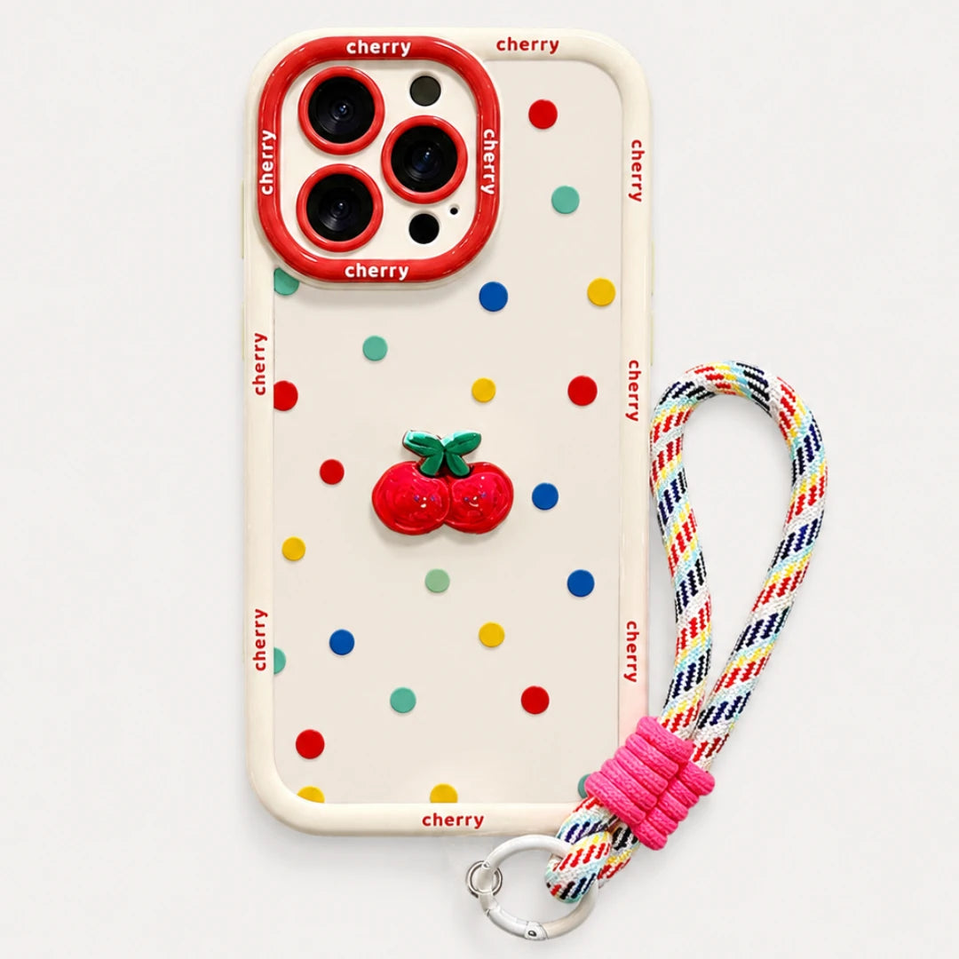 Josh & Tate - CherryPop™ iPhone Case - A cream-colored phone case decorated with colorful cherry-themed polka dots, a 3D red cherry accent, and a red camera bumper. It is shown with a matching multicolor woven wrist strap featuring a pink knotted section and a silver metal clasp, set against a plain light gray background.