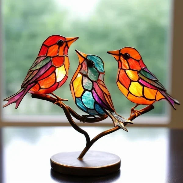 Colorful stained glass birds on a branch against a blurred window background