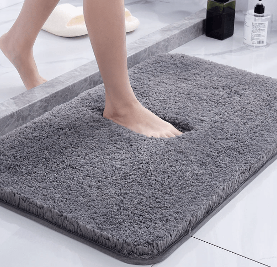 Person stepping onto a gray bath mat in a bathroom setting.