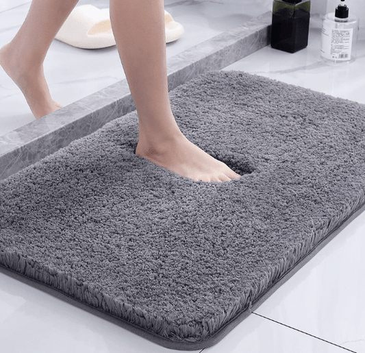 Person stepping onto a gray bath mat in a bathroom setting.