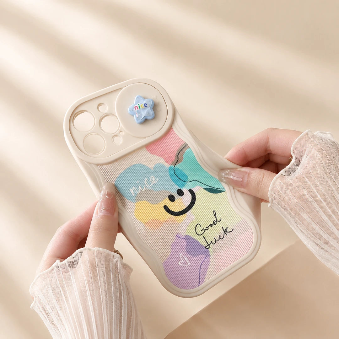 Josh & Tate - CloudPop™ Sliding Lens iPhone Case - A person holds a pastel-colored phone case with a colorful cloud design, smiley face, and the words 'Nice' and 'Good Luck'. The case has a beige bumper and camera cutout, and the person is wearing sheer white long-sleeve ruffled sleeves.