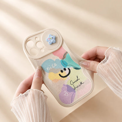 Josh & Tate - CloudPop™ Sliding Lens iPhone Case - A person holds a pastel-colored phone case with a colorful cloud design, smiley face, and the words 'Nice' and 'Good Luck'. The case has a beige bumper and camera cutout, and the person is wearing sheer white long-sleeve ruffled sleeves.