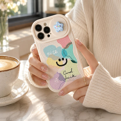 Josh & Tate - CloudPop™ Sliding Lens iPhone Case - A person in a cream ribbed sweater holds a pastel wavy phone case with a smiley face and colorful cloud graphics. The case has a small blue star-shaped camera accent.