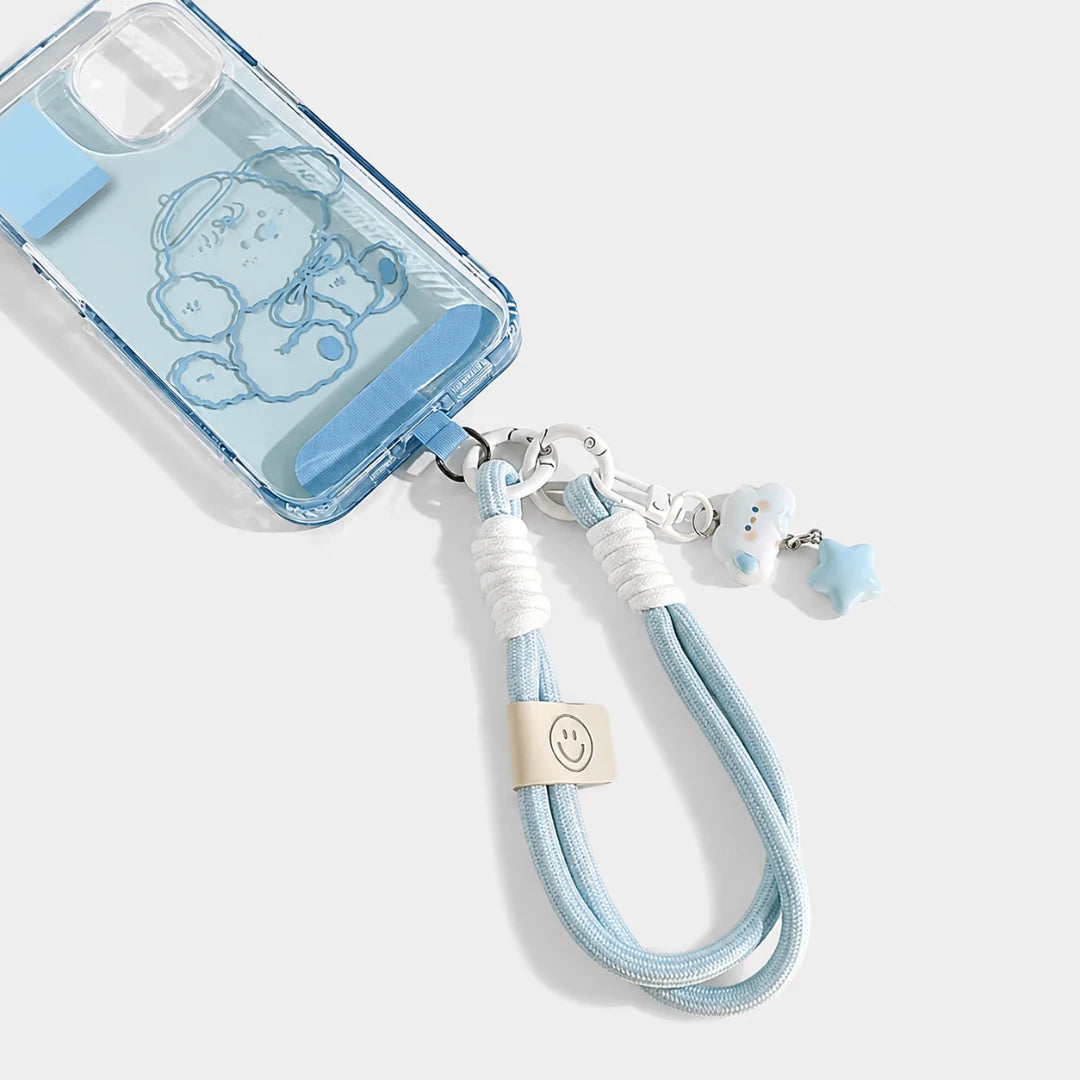 Josh & Tate - CloudStar™ Phone Lanyard - A clear light blue phone case with a cartoon character design, attached to a light blue wrist strap with white cord wraps, metal clips, and small character charms, shown on a light gray background.