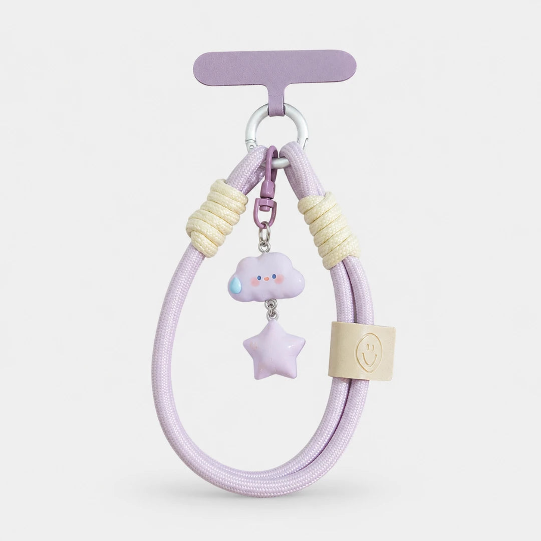 Josh & Tate - CloudStar™ Phone Lanyard - A pastel purple braided keychain or bag charm with cream rope wraps, a small lavender cloud charm with a blue tear drop, a lavender star charm, and a beige leather tag, displayed on a light gray background.