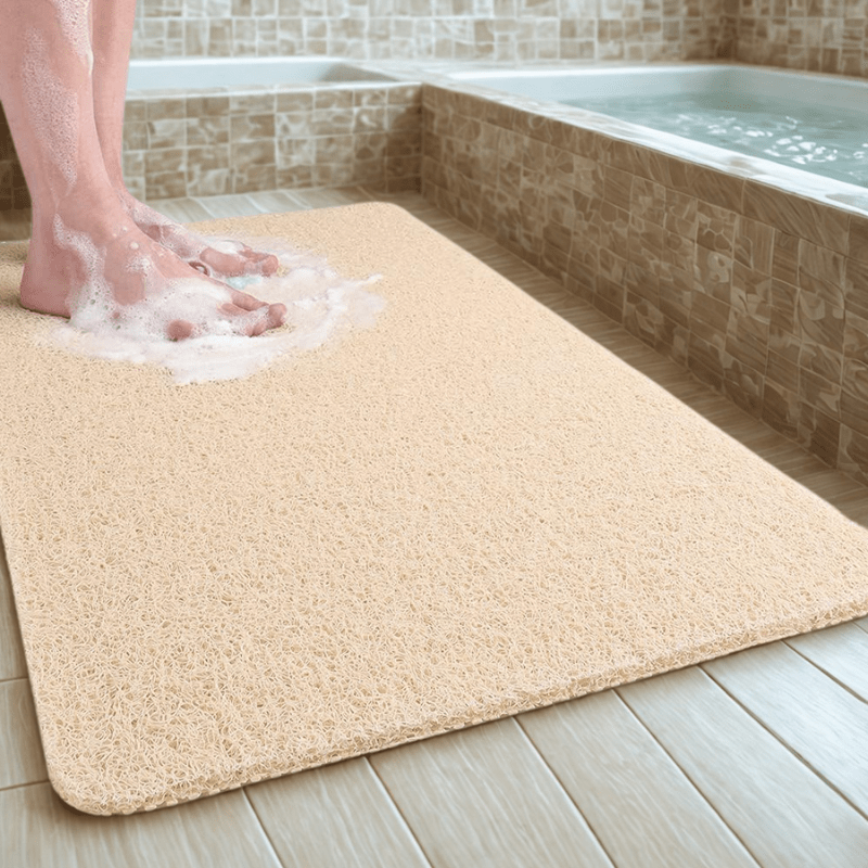 Beige bath mat on a bathroom floor with soapy water near a bathtub.