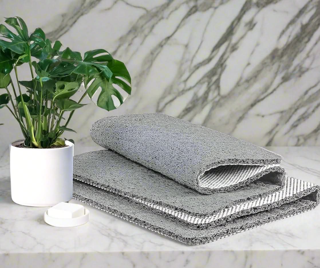 Three gray textured cloths stacked on a marble surface with a plant in the background