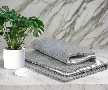 Three gray textured cloths stacked on a marble surface with a plant in the background