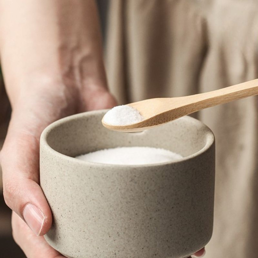 Person holding a ceramic bowl with a wooden spoon scooping salt.