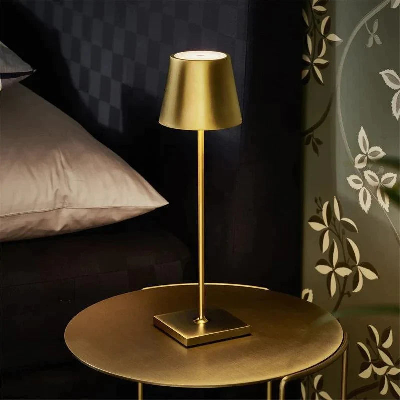 Gold table lamp on a round table against a dark wall with decorative elements.