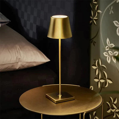 Gold table lamp on a round table against a dark wall with decorative elements.