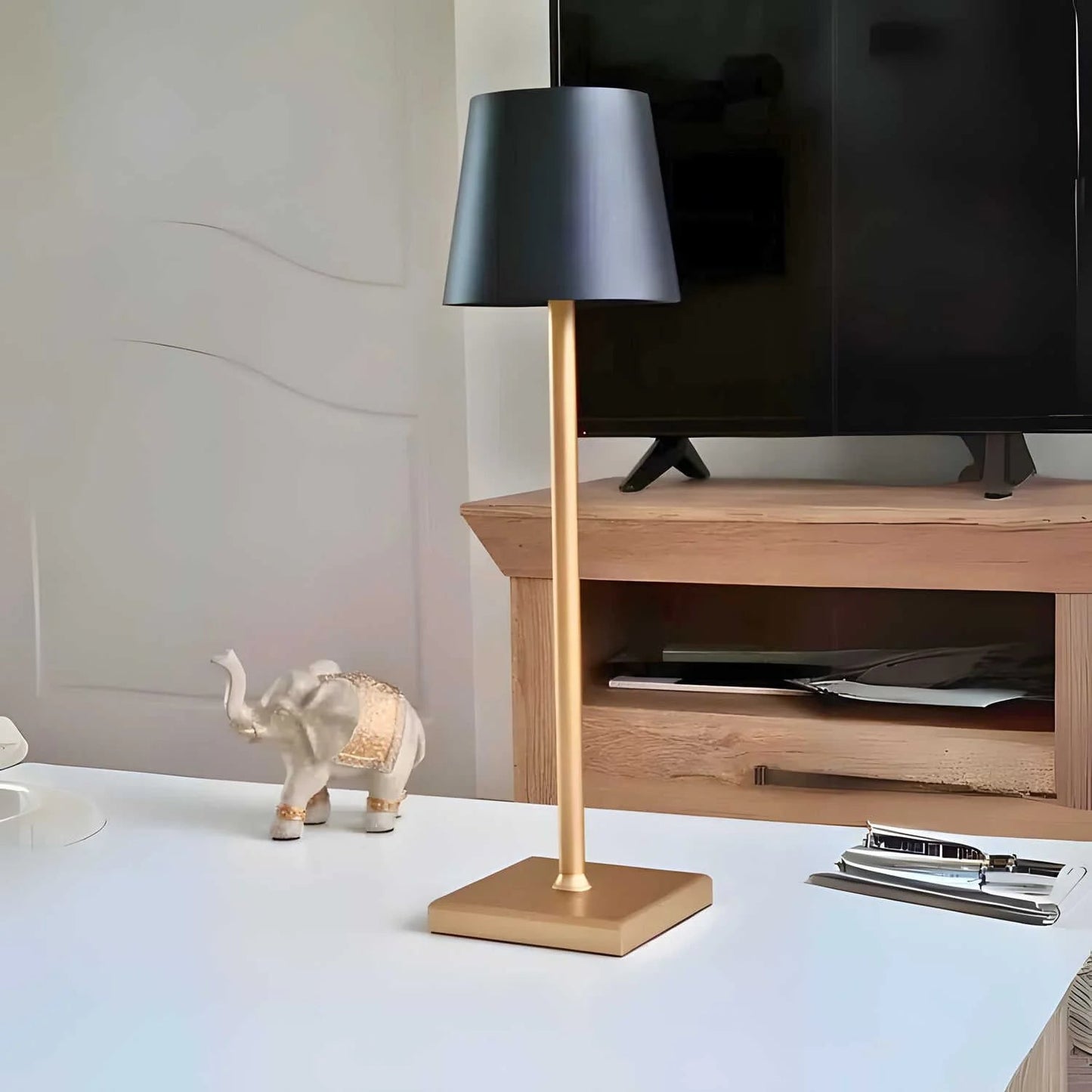 Table lamp with gold base and black shade on a desk next to a TV