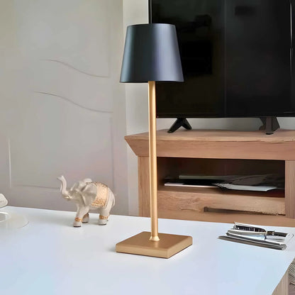 Table lamp with gold base and black shade on a desk next to a TV