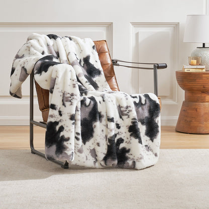 Black and white patterned blanket draped over a brown leather chair in a room with wooden flooring and a lamp.