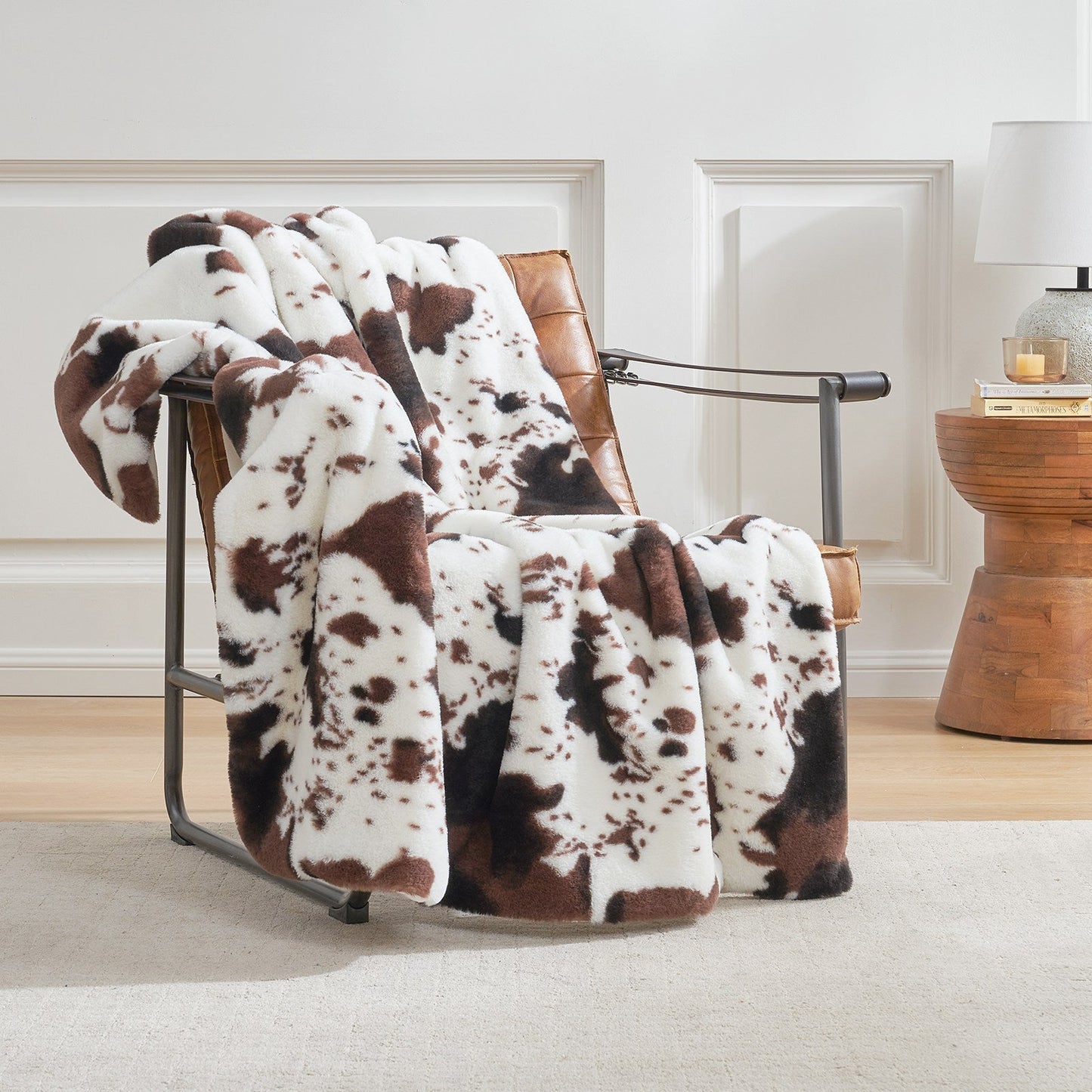 Brown and white cow print blanket draped over a chair in a room with a wooden side table.