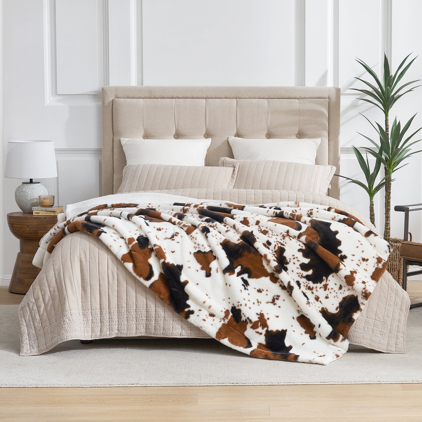Bed with cow print blanket and beige headboard in a room setting