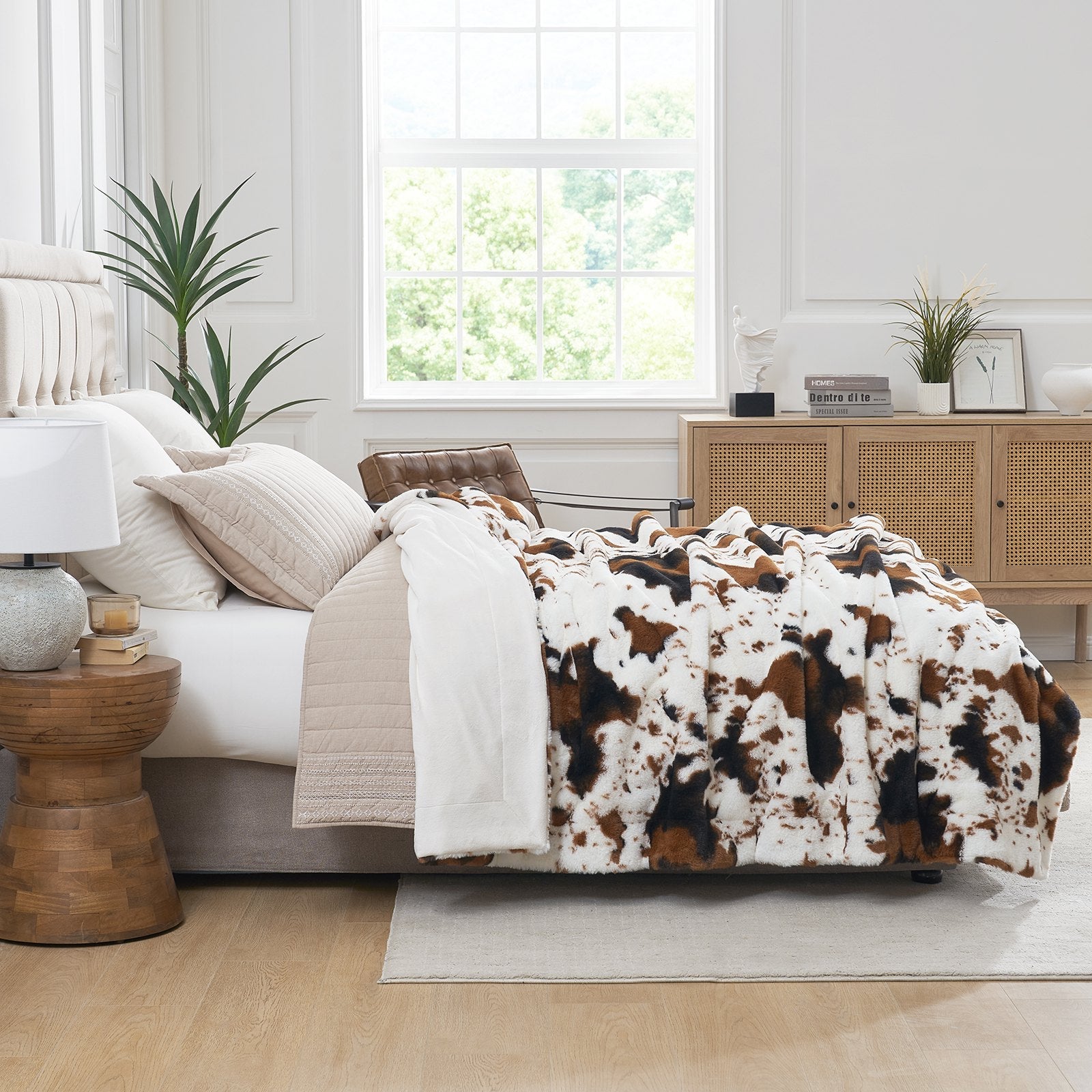 Bedroom with a bed featuring a cowhide patterned comforter, wooden side table, and window.