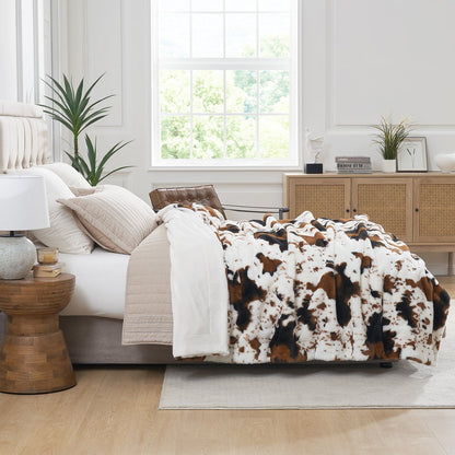 Bedroom with a bed featuring a cowhide patterned comforter, wooden side table, and window.