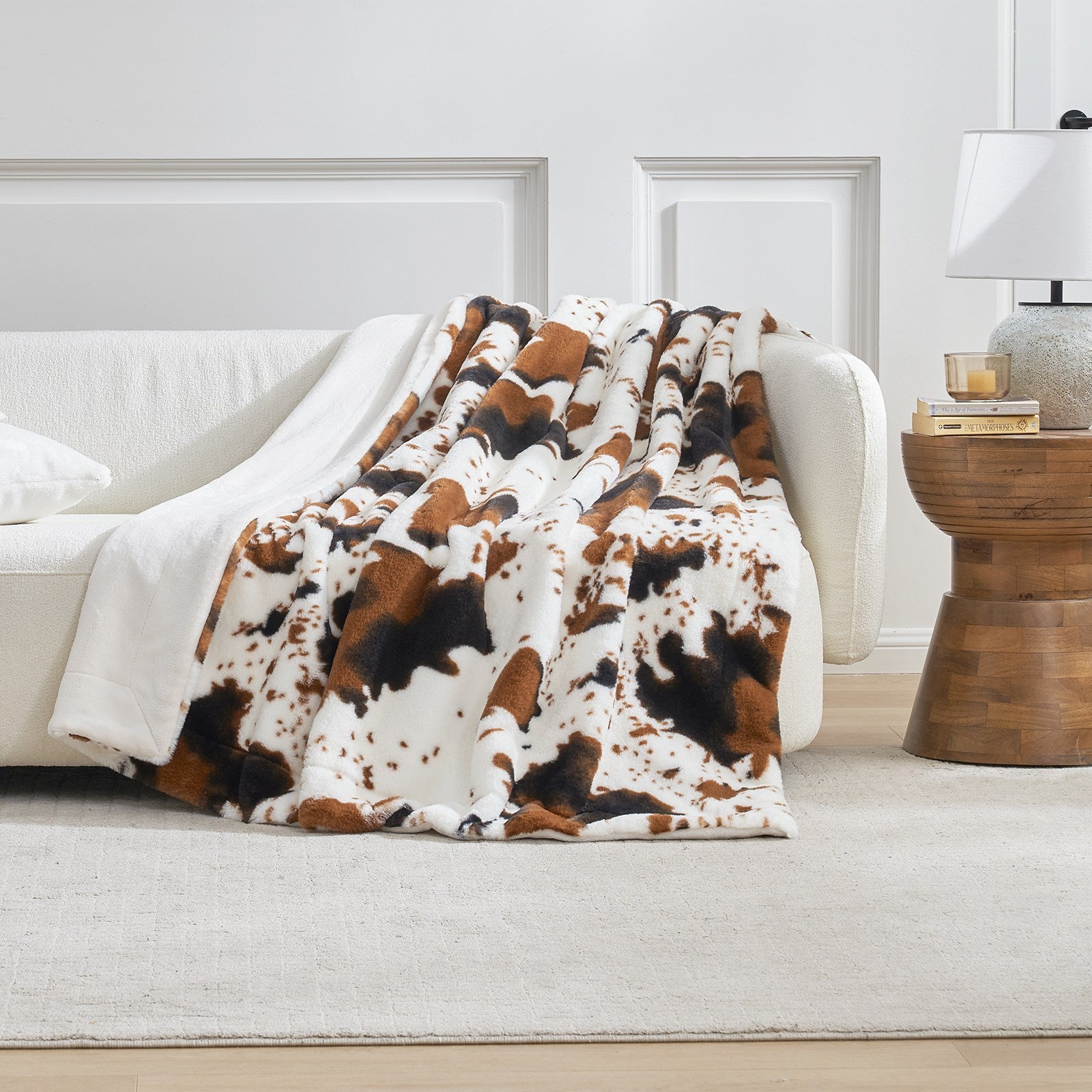 Cow print blanket draped over a white sofa in a living room setting.