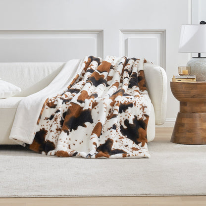 Cow print blanket draped over a white sofa in a living room setting.