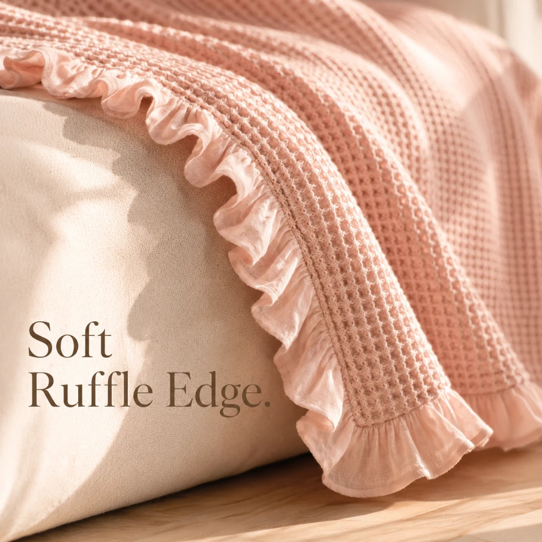 Josh & Tate - CozyCradle™ Ruffle-Edge Cotton Bed Blanket - Pink textured blanket with ruffle edge on a wooden surface