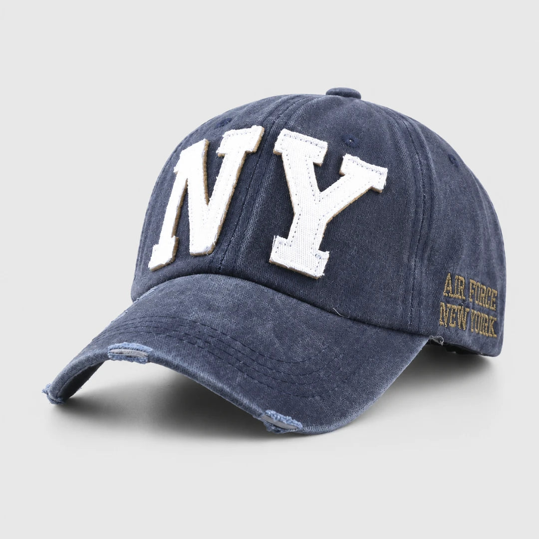 Josh & Tate - CraftWorn™ Distressed NY Cap - A navy blue distressed baseball cap featuring large white embroidered 'NY' letters on the front and gold embroidered 'AIR FORCE NEW YORK' text on the side, shown against a light gray background.