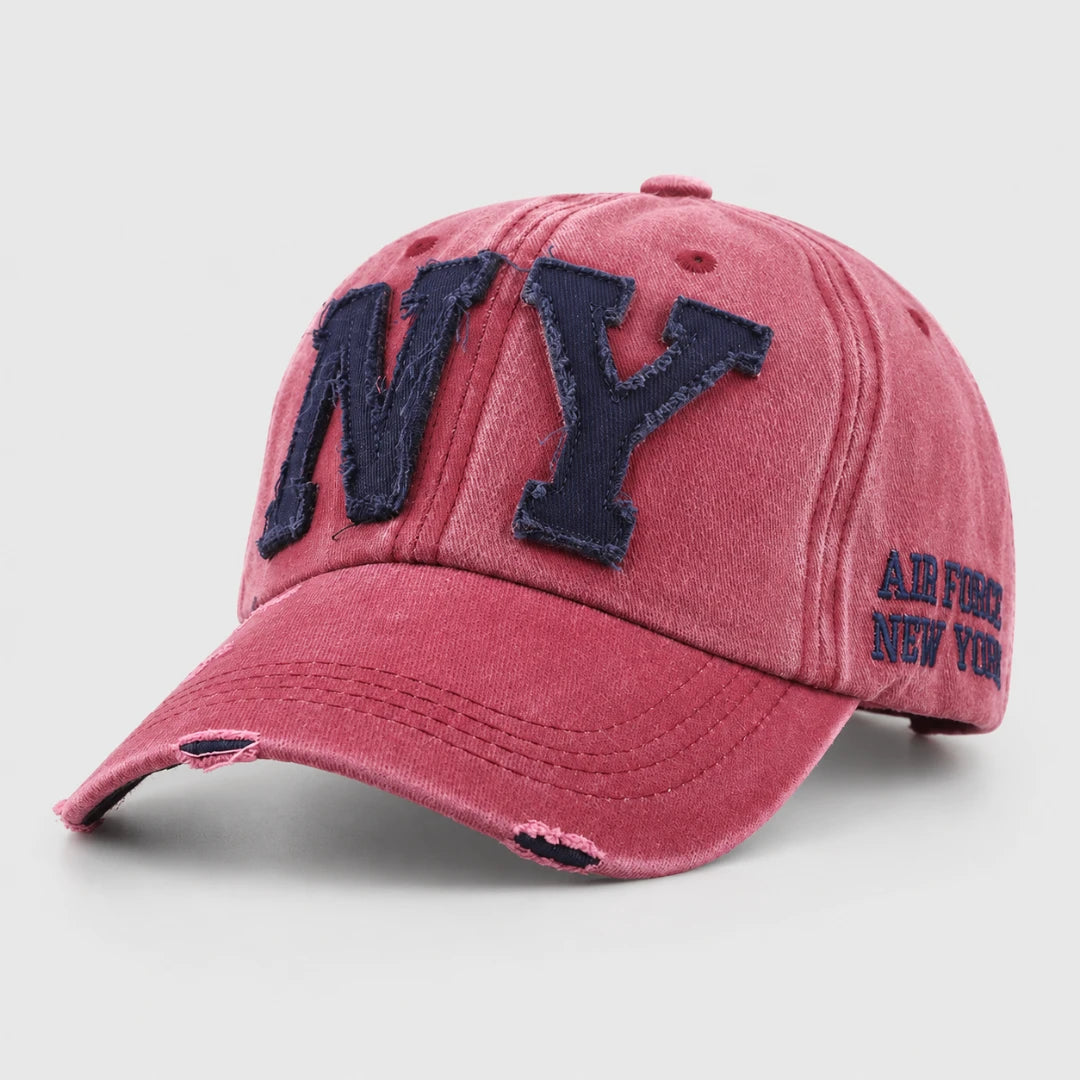 Josh & Tate - CraftWorn™ Distressed NY Cap - A distressed pink baseball cap with dark navy blue embroidered 'NY' lettering on the front and 'AIR FORCE NEW YORK' text on the side, shown on a light gray background.