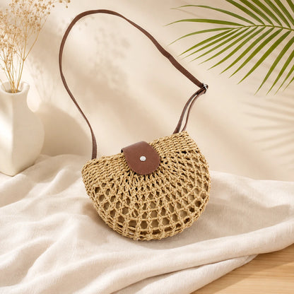 Josh & Tate - CrochetMoon™ Straw Crossbody Bag - Woven handbag with a brown leather patch on a light fabric surface with a plant in the background