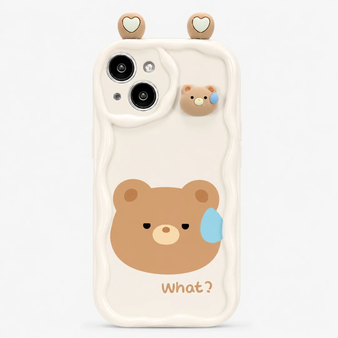 Josh & Tate - CuteSilicone™ iPhone Case - A cream-colored phone case featuring a cute cartoon bear face with a blue teardrop and the word 'What?' printed below. The case has wavy cutout lines around the camera and a small 3D bear ear accessory on top, set against a plain light gray background.