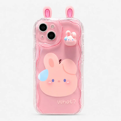 Josh & Tate - CuteSilicone™ iPhone Case - A pink phone case with a cute cartoon bunny design, featuring a large pink bunny face on the back, a smaller bunny charm on the upper right, and pink bunny ears protruding from the top. The case is transparent and has the word 'What?' printed near the bottom.