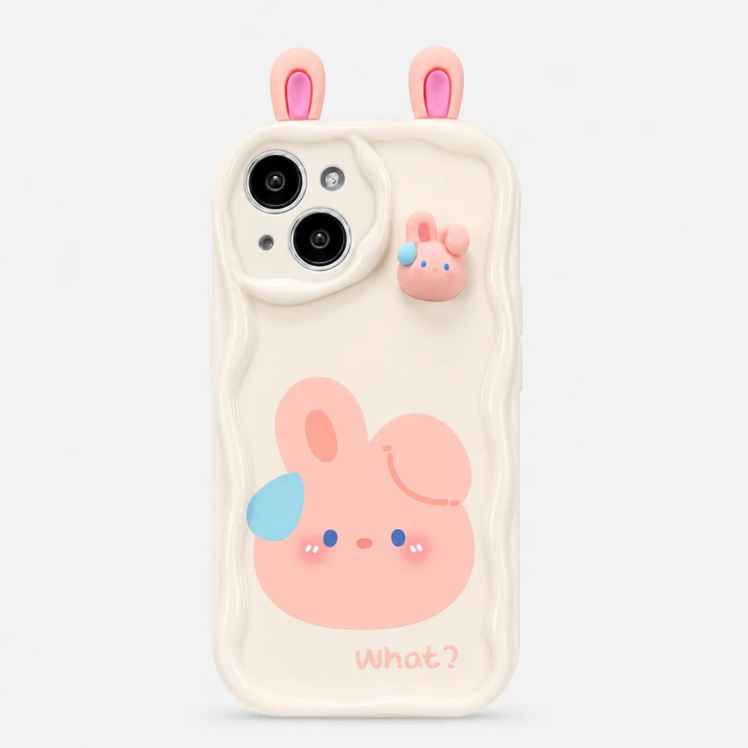 Josh & Tate - CuteSilicone™ iPhone Case - A cream-colored phone case with a cute pink bunny design, featuring a large pink bunny face with a blue ear, a small pink bunny charm on the upper right, and two pink bunny ears on top. The word 'What?' is printed at the bottom.