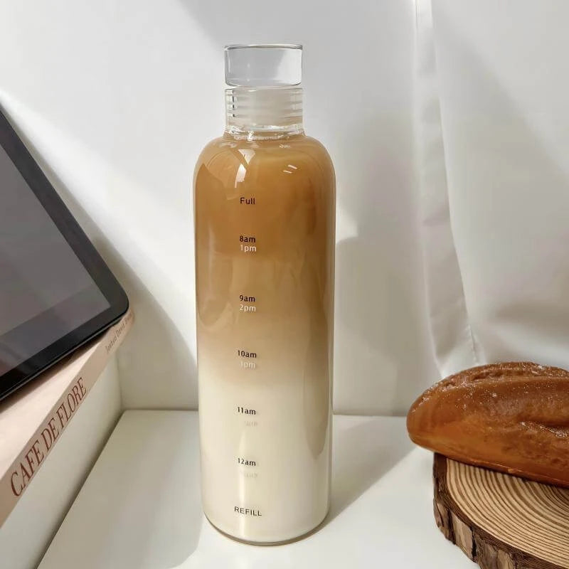 Josh & Tate - Daily Water Tracker Bottle - Gradient bottle with measurement scale on a white surface next to a book and bread
