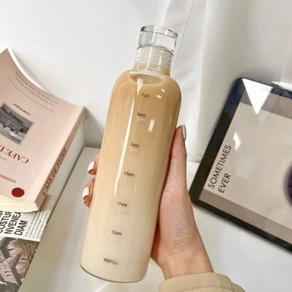 Josh & Tate - Daily Water Tracker Bottle - Hand holding a beige water bottle with measurement markings on a surface with books and a tablet.