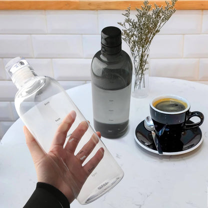 Josh & Tate - Daily Water Tracker Bottle - Hand holding a clear bottle with a black lid on a kitchen counter with a coffee cup and vase.