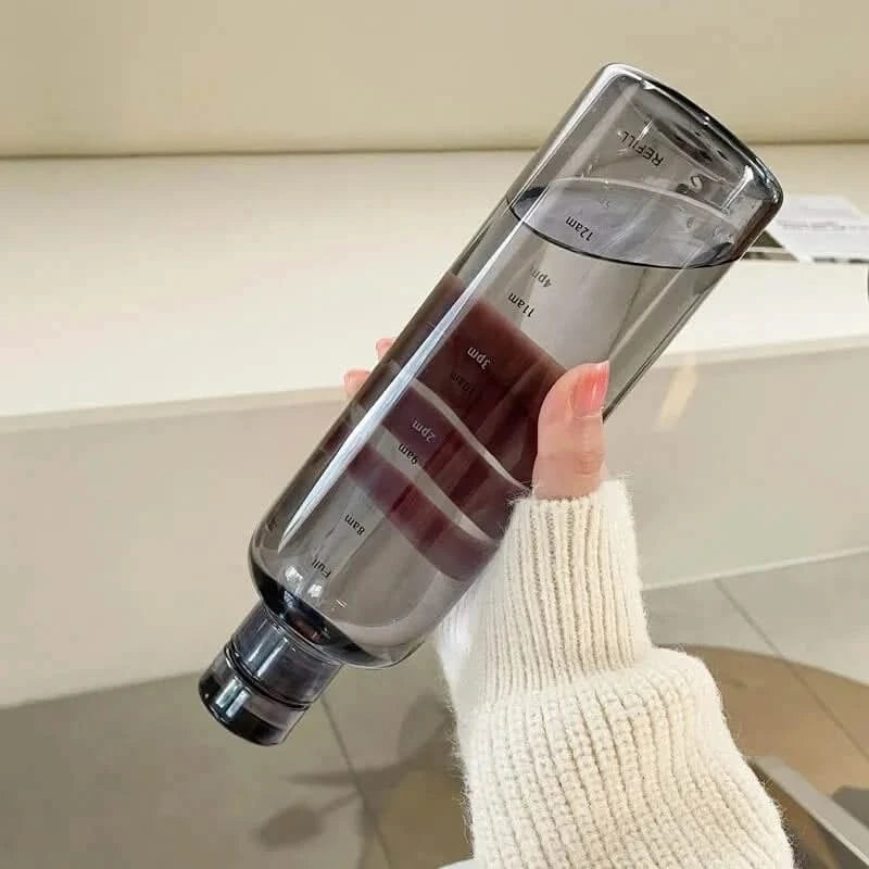 Josh & Tate - Daily Water Tracker Bottle - Clear water bottle with measurement markings held by a person wearing a white sweater.
