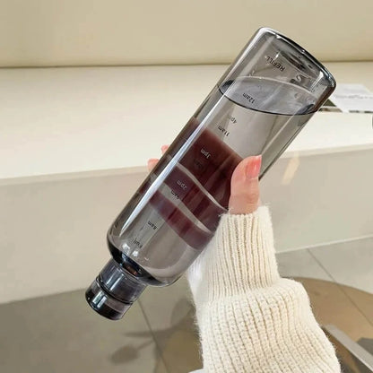 Josh & Tate - Daily Water Tracker Bottle - Clear water bottle with measurement markings held by a person wearing a white sweater.