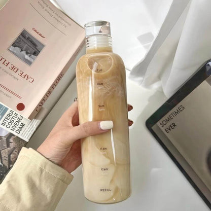 Josh & Tate - Daily Water Tracker Bottle - Hand holding a clear bottle with a liquid level indicator on a desk with books and a tablet.
