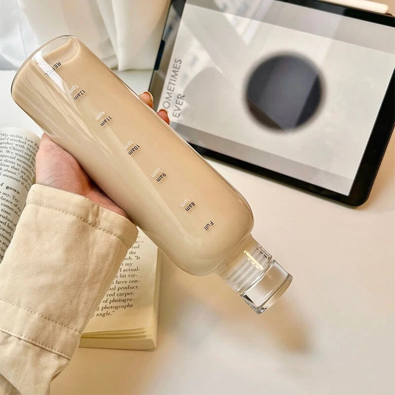 Josh & Tate - Daily Water Tracker Bottle - Beige water bottle held by a hand with an open book and tablet in the background
