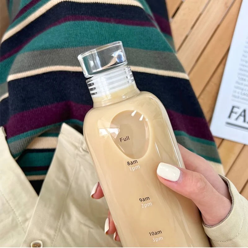 Josh & Tate - Daily Water Tracker Bottle - Hand holding a beige bottle with time markings against a striped fabric background