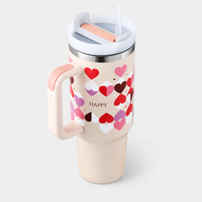 Josh & Tate - DayCarry™ 40oz Insulated Tumbler - A cream-colored insulated travel tumbler with a pink handle and lid, decorated with a pattern of red, pink, and white hearts, and the word 'HAPPY' printed on the front. It features a stainless steel rim and a white lid with a clear straw.