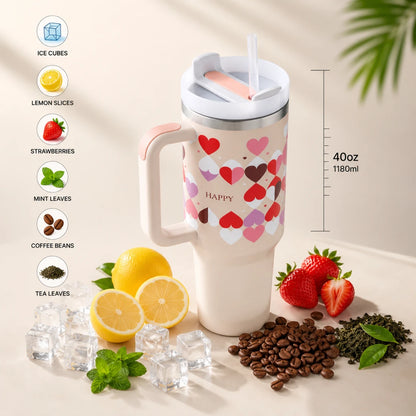 A 40 oz insulated travel tumbler with a handle, featuring a white body decorated with a colorful heart pattern and the word 'HAPPY' on the front. The tumbler is shown with a clear lid and straw, surrounded by ice cubes, lemons, strawberries, coffee beans, and mint leaves.