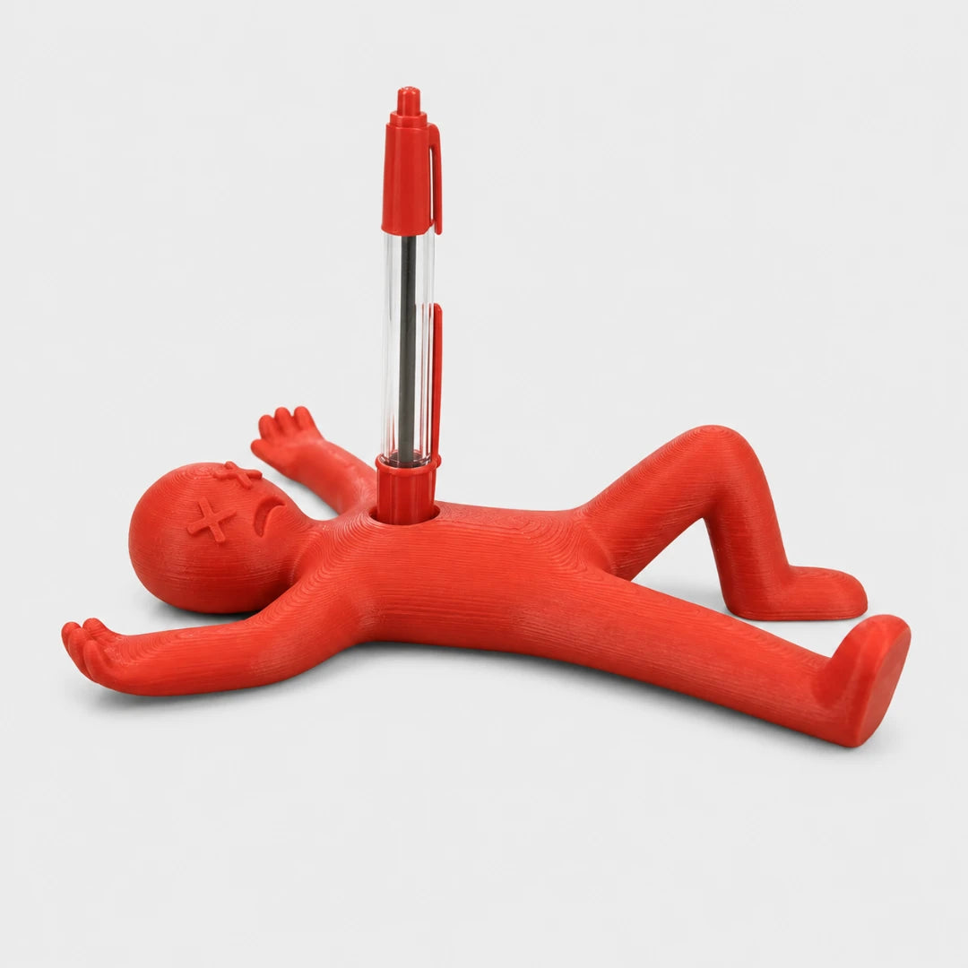 Josh & Tate - DeadDrop™ Desk Pen Stand - A red novelty pen holder shaped like a lying figure, with a pen inserted vertically into the center back, photographed on a clean light gray studio background.