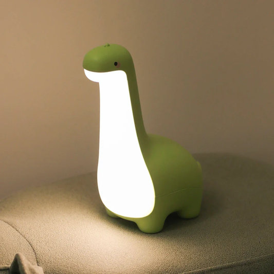 Green dinosaur-shaped night light on a beige surface with a neutral background