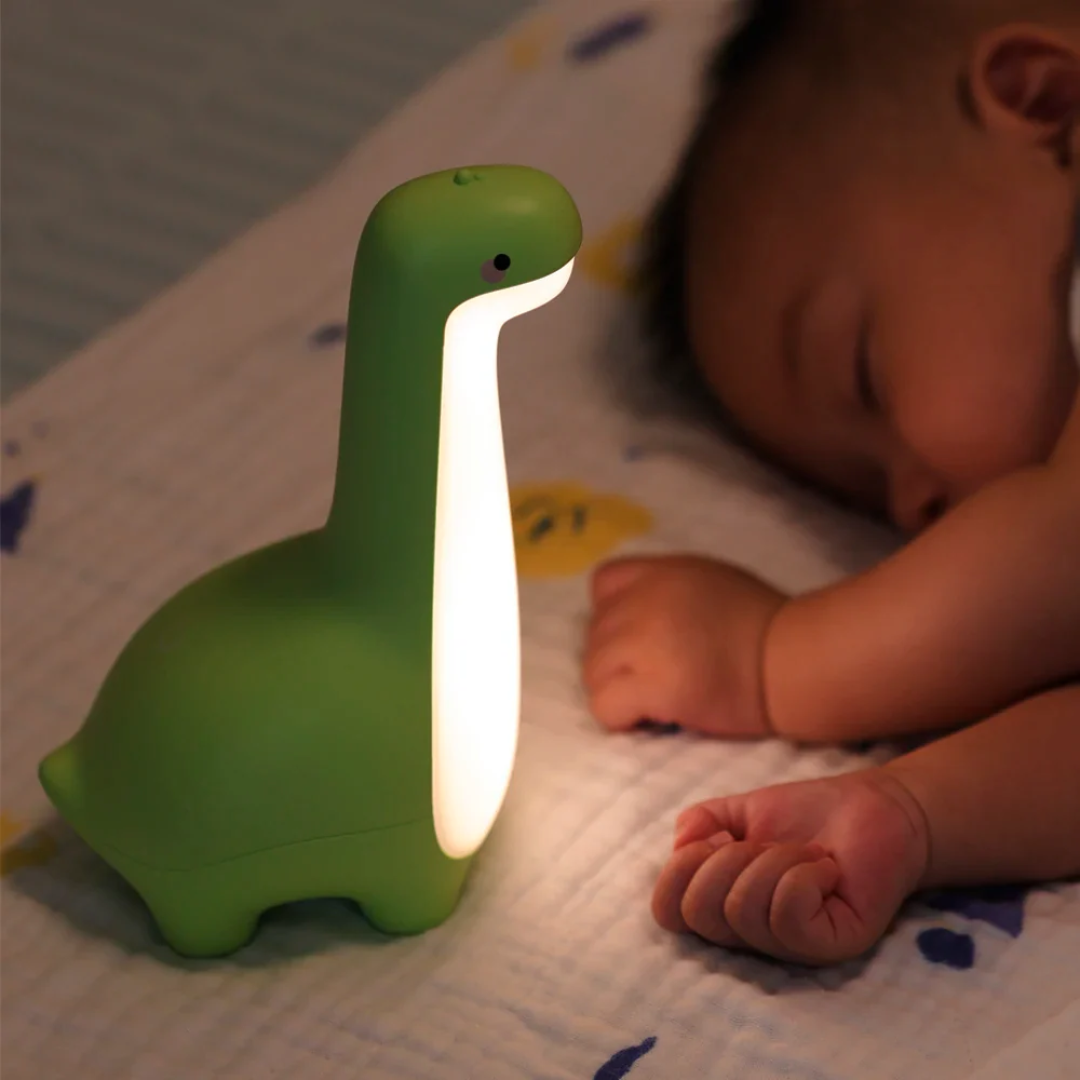 Green dinosaur-shaped night light next to a sleeping baby