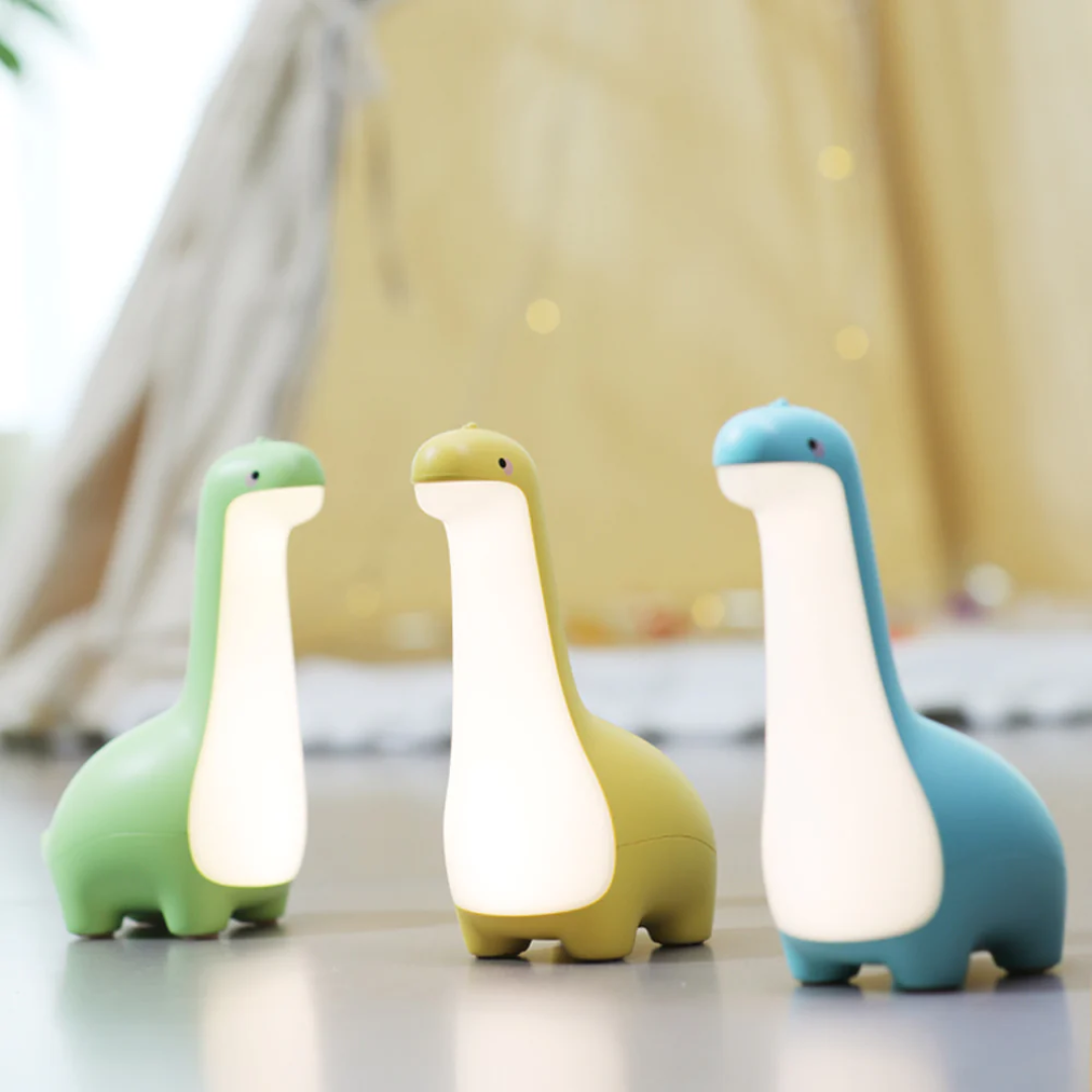 Three dinosaur-shaped night lights in green, yellow, and blue on a light surface.
