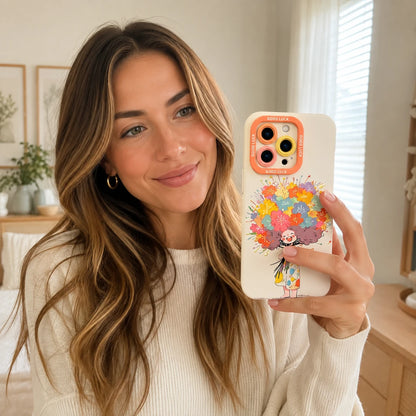 Josh & Tate - DoodleBloom™ iPhone Case - A woman holding a white phone case with a colorful floral illustration and an orange camera bumper, photographed in a bright indoor room.