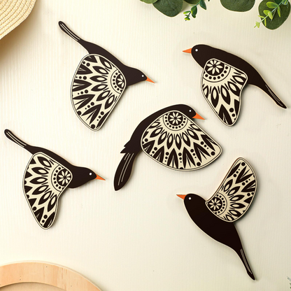 Decorative black and white bird-shaped coasters on a light surface with green leaves in the background.
